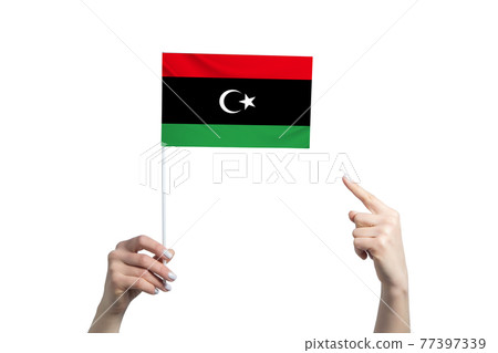 A beautiful female hand holds a Libya flag to which she shows the finger of her other hand, isolated on white background 77397339