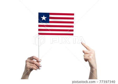 A beautiful female hand holds a Liberia flag to which she shows the finger of her other hand, isolated on white background A beautiful female hand holds a Liberia flag to which she shows the finger of her other hand, isolated on white background 77397340