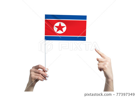 A beautiful female hand holds a North Korea flag to which she shows the finger of her other hand, isolated on white background A beautiful female hand holds a North Korea flag to which she shows the finger of her other hand, isolated on white background 77397349