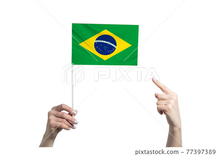 A beautiful female hand holds a Brazil flag to which she shows the finger of her other hand, isolated on white background 77397389