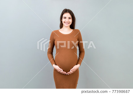 Happy pregnant woman touching her abdomen at Colored background. Future mother is wearing white underwear. Expecting of a baby. Copy space Happy pregnant woman touching her abdomen at Colored background. Future mother is wearing white underwear. Expecting of a baby. Copy space 77398687