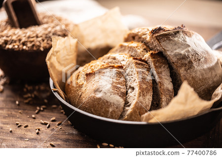 Lovely crunchy yeast bread slices served on the baking paper in the alloy rustic pan on the wooden table with whole wheat grains in the background Lovely crunchy yeast bread slices served on the baking paper in the alloy rustic pan on the wooden table with whole wheat grains in the background 77400786