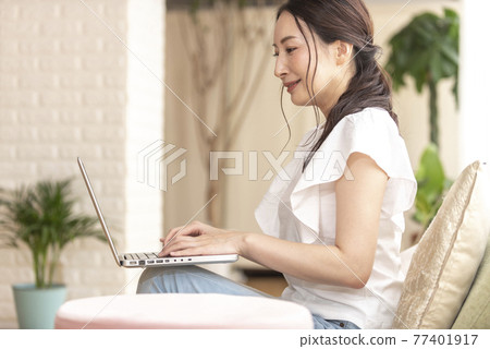 一個女人坐在家裡操作電腦 77401917