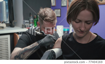 Photo of man doing black tattoo on woman in studio Photo of man doing black tattoo on woman in studio 77404169