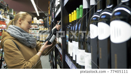 Woman in the store choosing bottle of wine 77405111