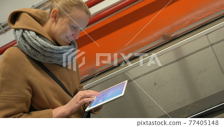 Woman on escalator using tablet computer 77405148