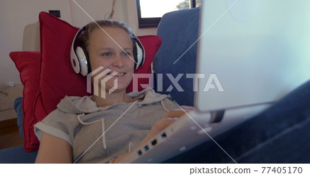 Woman in headphones with laptop on the sofa Woman in headphones with laptop on the sofa 77405170