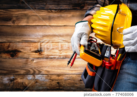 Electrician technician with tool belt on rustic wooden background. Electricity. 77408006