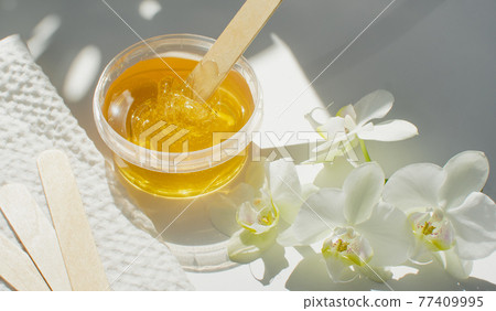 Sugar paste or wax honey in a transparent jar on a white background. Sugaring. Depilation and beauty concept. Waxing. 77409995