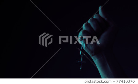 Praying with a rosary. hand of Catholic man with rosary on black background. Hands holding a silver rosary or cross pendant of Jesus Christ. Crucifix and hand on black background. Praying God concept Praying with a rosary. hand of Catholic man with rosary on black background. Hands holding a silver rosary or cross pendant of Jesus Christ. Crucifix and hand on black background. Praying God concept 77410370