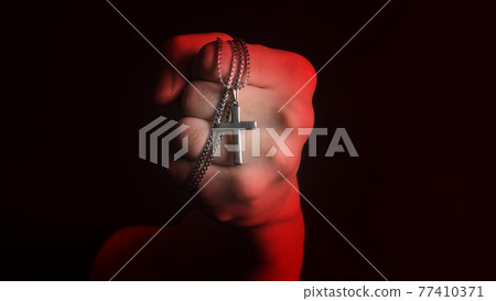 Praying with a rosary. hand of Catholic man with rosary on black background. Hands holding a silver rosary or cross pendant of Jesus Christ. Crucifix and hand on black background. Praying God concept 77410371