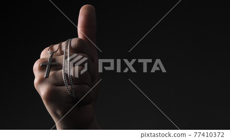 Praying with a rosary. hand of Catholic man with rosary on black background. Hands holding a silver rosary or cross pendant of Jesus Christ. Crucifix and hand on black background. Praying God concept Praying with a rosary. hand of Catholic man with rosary on black background. Hands holding a silver rosary or cross pendant of Jesus Christ. Crucifix and hand on black background. Praying God concept 77410372