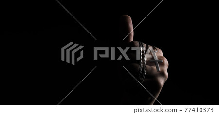 Praying with a rosary. hand of Catholic man with rosary on black background. Hands holding a silver rosary or cross pendant of Jesus Christ. Crucifix and hand on black background. Praying God concept Praying with a rosary. hand of Catholic man with rosary on black background. Hands holding a silver rosary or cross pendant of Jesus Christ. Crucifix and hand on black background. Praying God concept 77410373