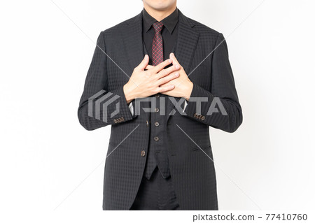 A male businessman standing in front of a white background and putting his hand on his chest 77410760