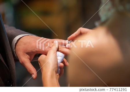 Closeup of bride putting a wedding ring onto the groom's finger. Couple exchanging wedding rings. Closeup of bride putting a wedding ring onto the groom's finger. Couple exchanging wedding rings. 77411291