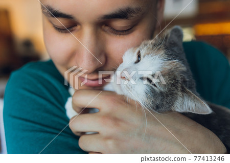 Young man in t shirt holding a cat. 77413246