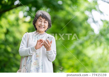 A senior woman who operates a smartphone, an old woman who touches a smartphone outdoors 77415139