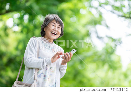 一位操作智能手機的老婦人，一位在戶外觸摸智能手機的老婦人 77415142