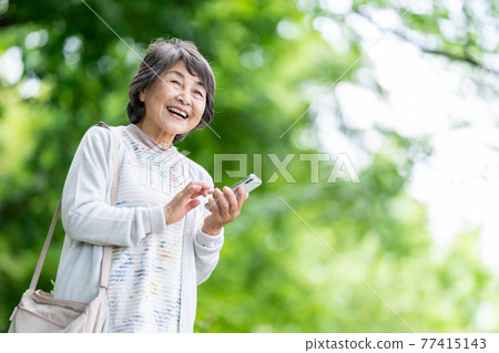 A senior woman who operates a smartphone, an old woman who touches a smartphone outdoors 77415143