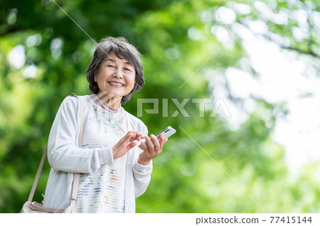 一位操作智能手機的老婦人，一位在戶外觸摸智能手機的老婦人 77415144