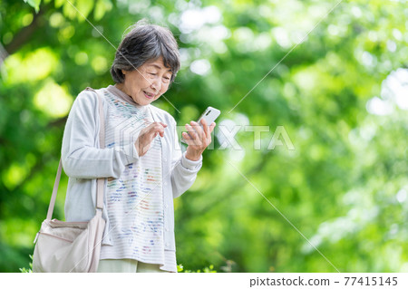 一位操作智能手機的老婦人，一位在戶外觸摸智能手機的老婦人 77415145