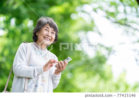 一位操作智能手機的老婦人，一位在戶外觸摸智能手機的老婦人 77415146