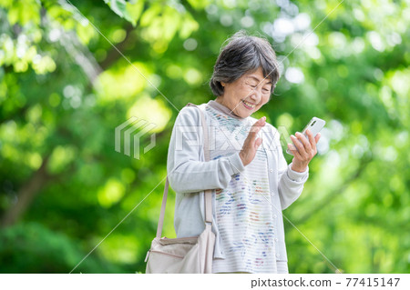 一位操作智能手機的老婦人，一位在戶外觸摸智能手機的老婦人 77415147