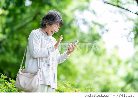 A senior woman who operates a smartphone, an old woman who touches a smartphone outdoors 77415153