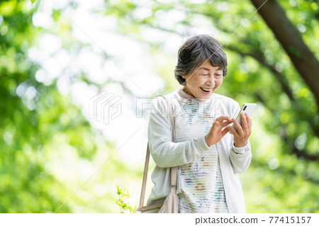 A senior woman who operates a smartphone, an old woman who touches a smartphone outdoors 77415157