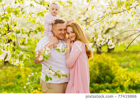family with a baby daughter in spring flowering garden. cleft lip in infants. family with a baby daughter in spring flowering garden. cleft lip in infants. 77419866