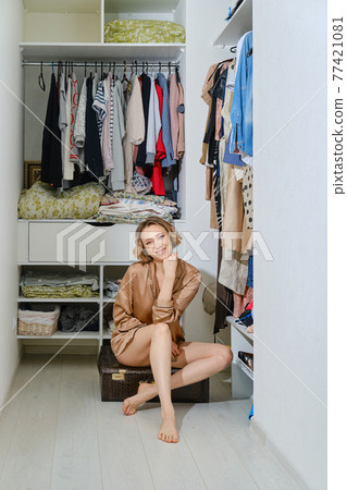 Happy woman sits on a suitcase in dressing room 77421081