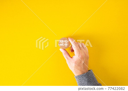 Male hand holds a wooden block with the word apply now on yellow background. 77422082