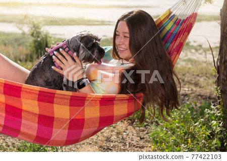 girl outdoors, lies in a hammock and holds a miniature schnauzer dog in her arms, emotions girl outdoors, lies in a hammock and holds a miniature schnauzer dog in her arms, emotions 77422103