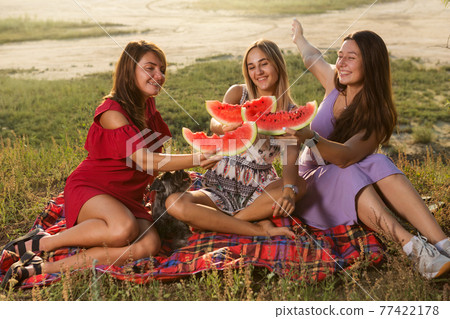 three girlfriends and a small dog on a picnic, eating watermelon and having fun, emotions and gestures, lifestyle three girlfriends and a small dog on a picnic, eating watermelon and having fun, emotions and gestures, lifestyle 77422178