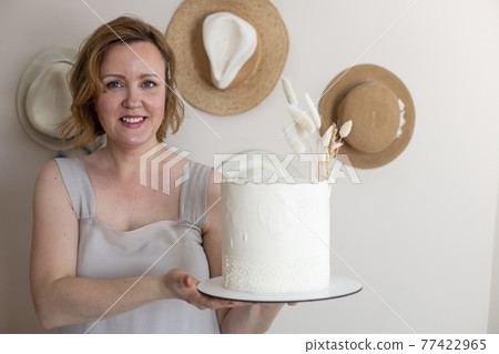 Happy elegant woman posing with tasty fresh cake cream beige decorated in boho scandi style Happy elegant woman posing with tasty fresh cake cream beige decorated in boho scandi style 77422965