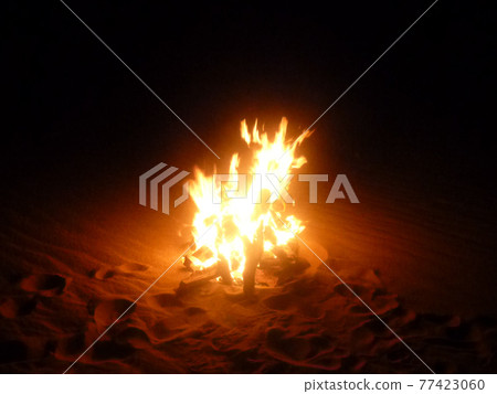 Burning flames at a campfire in the sand at night 77423060