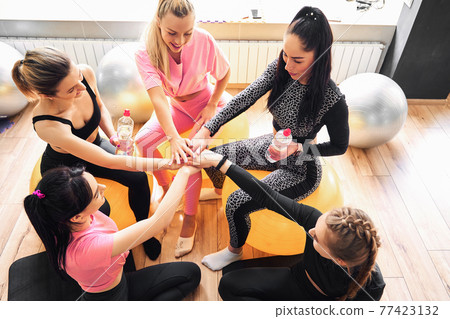 Group of fit happy people giving high five in fitness studio room, talking in a circle after seminar training. 77423132