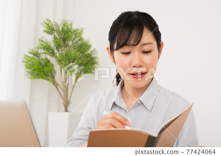 A woman who works while holding a pen and a notebook in front of a computer 77424064