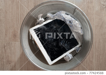 Modern tablet with highly broken screen in the litter bin. Close-up. 77424588