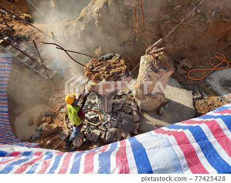 SEREMBAN, MALAYSIA -MARCH 05, 2021: Construction workers cutting concrete bore pile up to the determined level at the construction site. Stage fo work before fabricating the pile cap. SEREMBAN, MALAYSIA -MARCH 05, 2021: Construction workers cutting concrete bore pile up to the determined level at the construction site. Stage fo work before fabricating the pile cap. 77425428