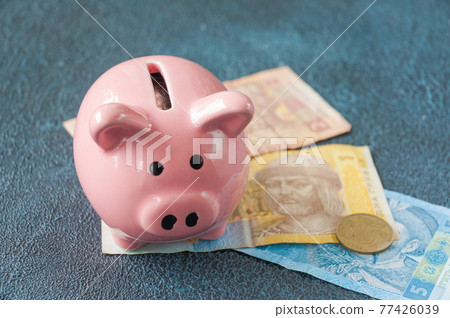 pink piggy bank with Ukrainian banknotes and coins 77426039