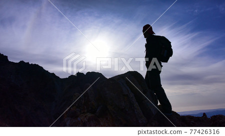 Silhouette of a man climbing a steep rocky mountain 77426316