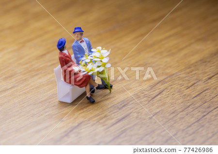Couple sitting on a bench with a white bouquet Couple sitting on a bench with a white bouquet 77426986