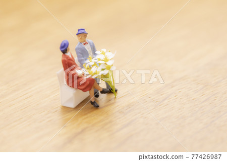 Couple sitting on a bench with a white bouquet 77426987