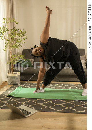 Woman repeating exercises while watching online workout session at home Woman repeating exercises while watching online workout session at home 77427516