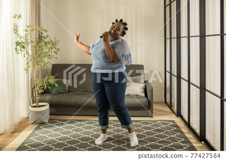 Multiracial woman holding microphone while singing at karaoke at home Multiracial woman holding microphone while singing at karaoke at home 77427584