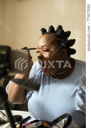 Blogger preparing makeup while sitting in front of smartphone at the tripod 77427680