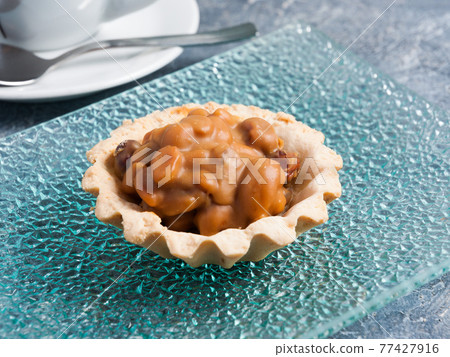 basket with nuts and caramel on a glass plate with a Cup of tea 77427916