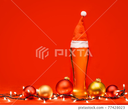 Tall glass of pale ale or beer with red santa hat christmas baubles and lights - christmas drink background Tall glass of pale ale or beer with red santa hat christmas baubles and lights - christmas drink background 77428023
