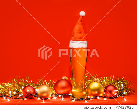 Tall glass of pale ale or beer with red santa hat christmas baubles tinsel and lights - christmas drink background Tall glass of pale ale or beer with red santa hat christmas baubles tinsel and lights - christmas drink background 77428026